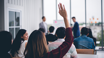 A woman raises her hand to ask a question at a public event