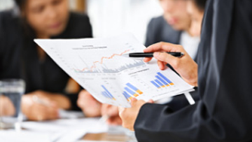 Someone reviews a sheet with different graphs on it, while others work in the background