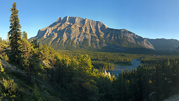 Vue d’une montagne et d’un cours d’eau, avec une forêt à l’avant-plan.