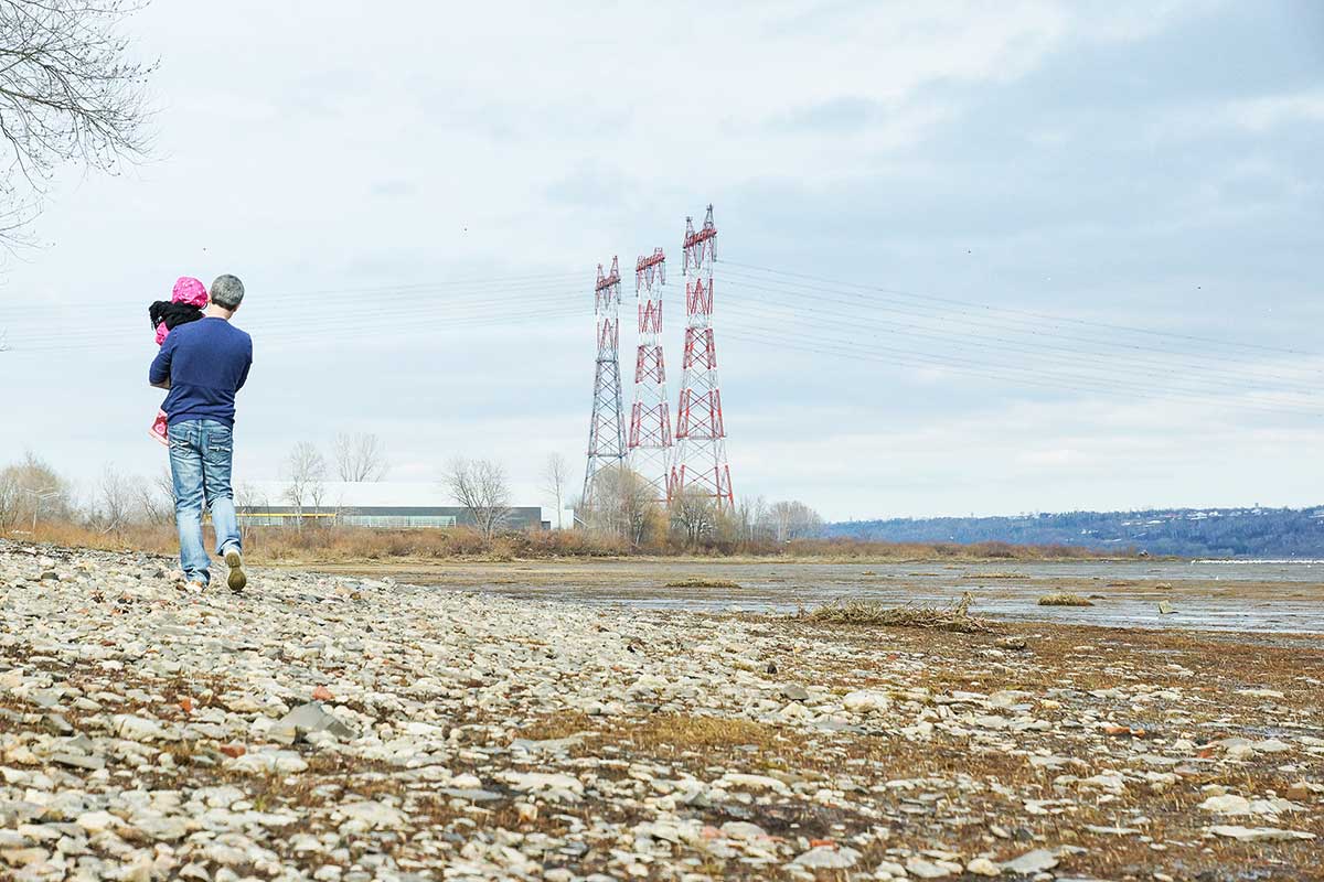 Figure&nbsp;1 &ndash; On the bank of a waterway, a man walks with a child in the direction of three electricity pylons.