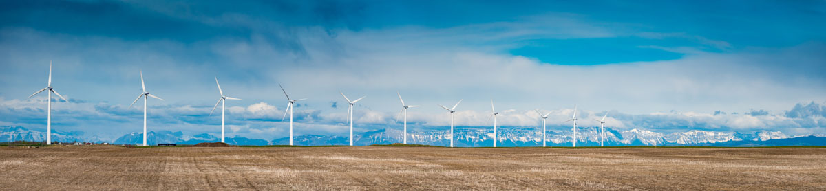Une rangée d’éoliennes dans un champ devant les Rocheuses.
