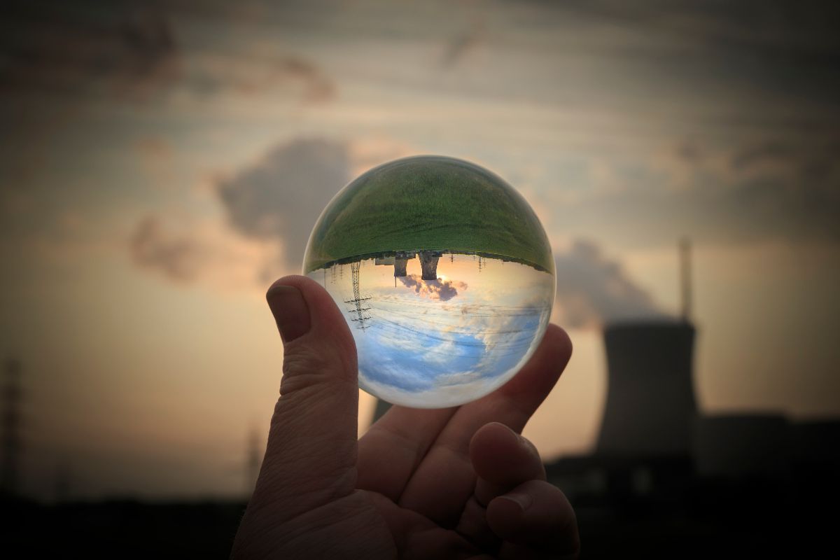 Main tenant un globe de verre dans lequel est reflétée une centrale nucléaire.