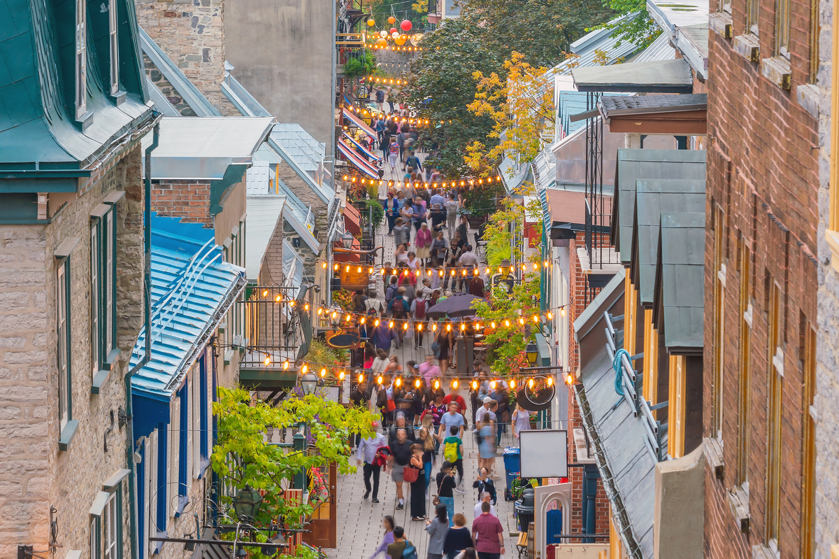 View from above a busy shopping district in Quebec, market lights shine above the heads of people walking below.