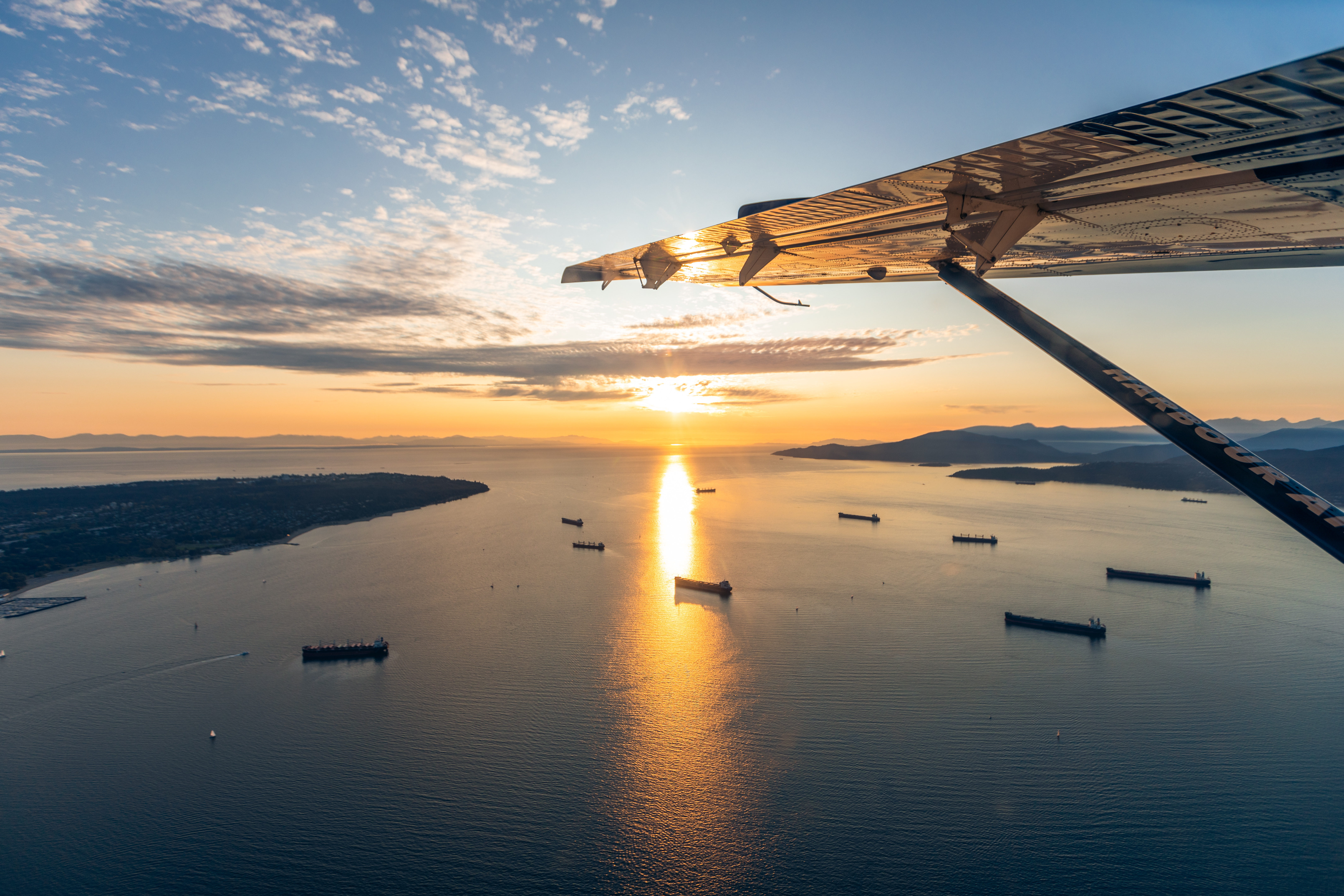 Harbour Air airplane wing detail flying over English Bay at sunset with tankers anchored on the water below.