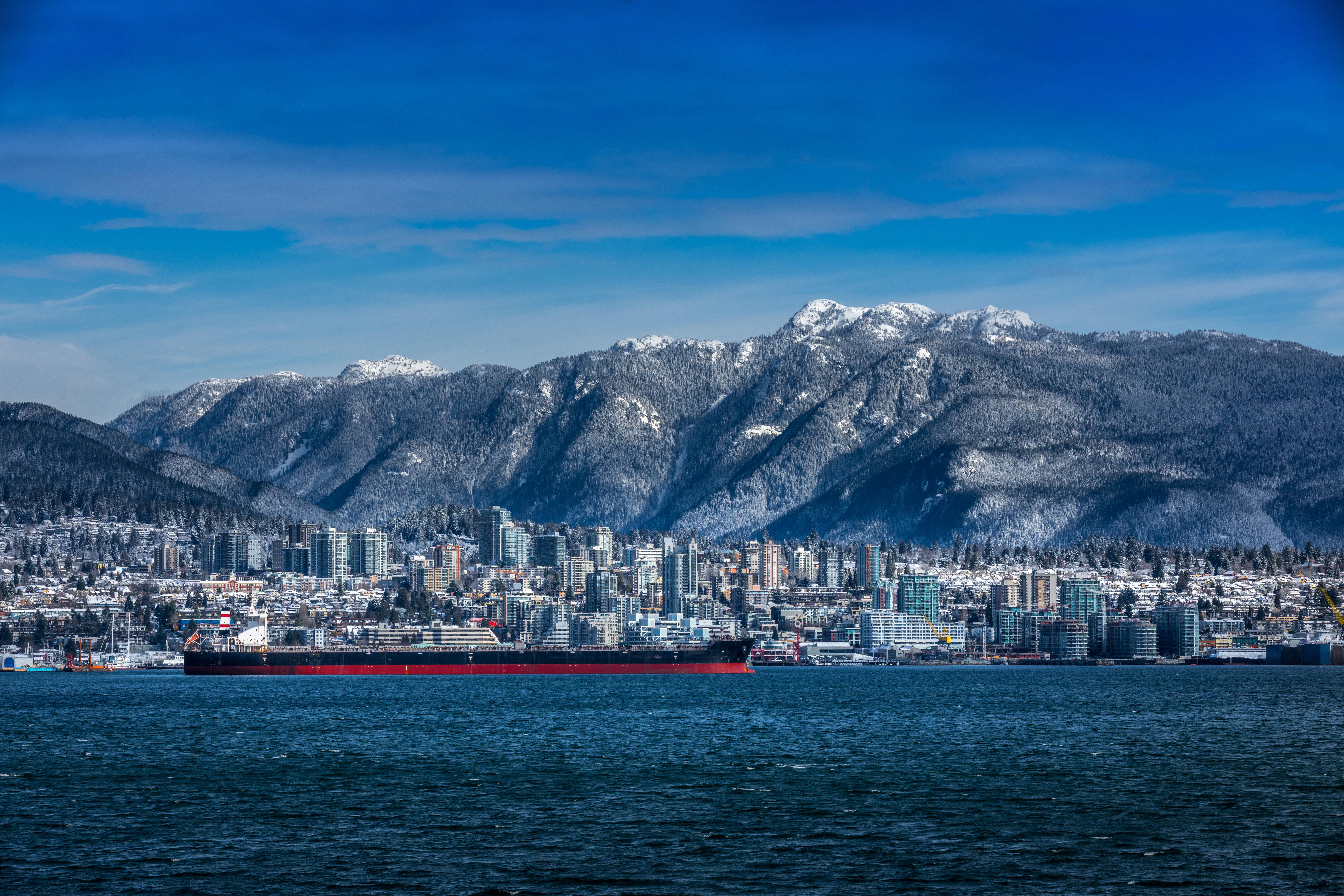 Tanker on the water in front of the North Vancouver skyline and snow dusted Rocky Mountains behind.