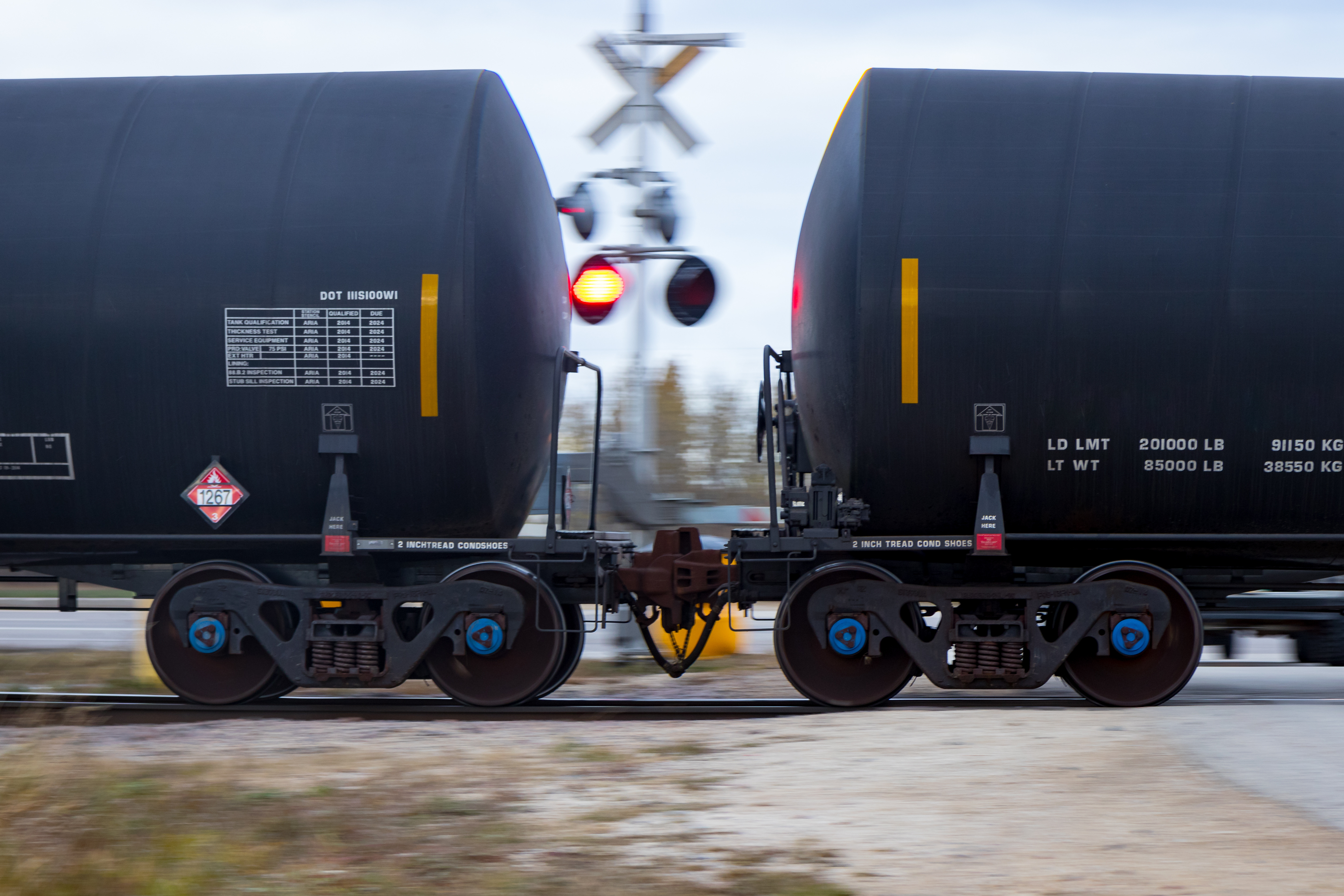 Connected crude oil rail tank cars passing a flashing railway crossing.