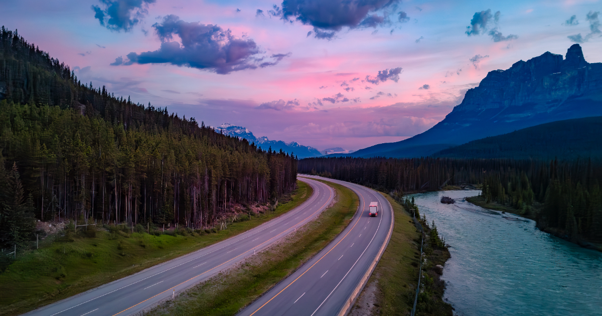A transport truck drives out of frame on the Trans-Canada highway in the Canadian Rockies as the sun rises.