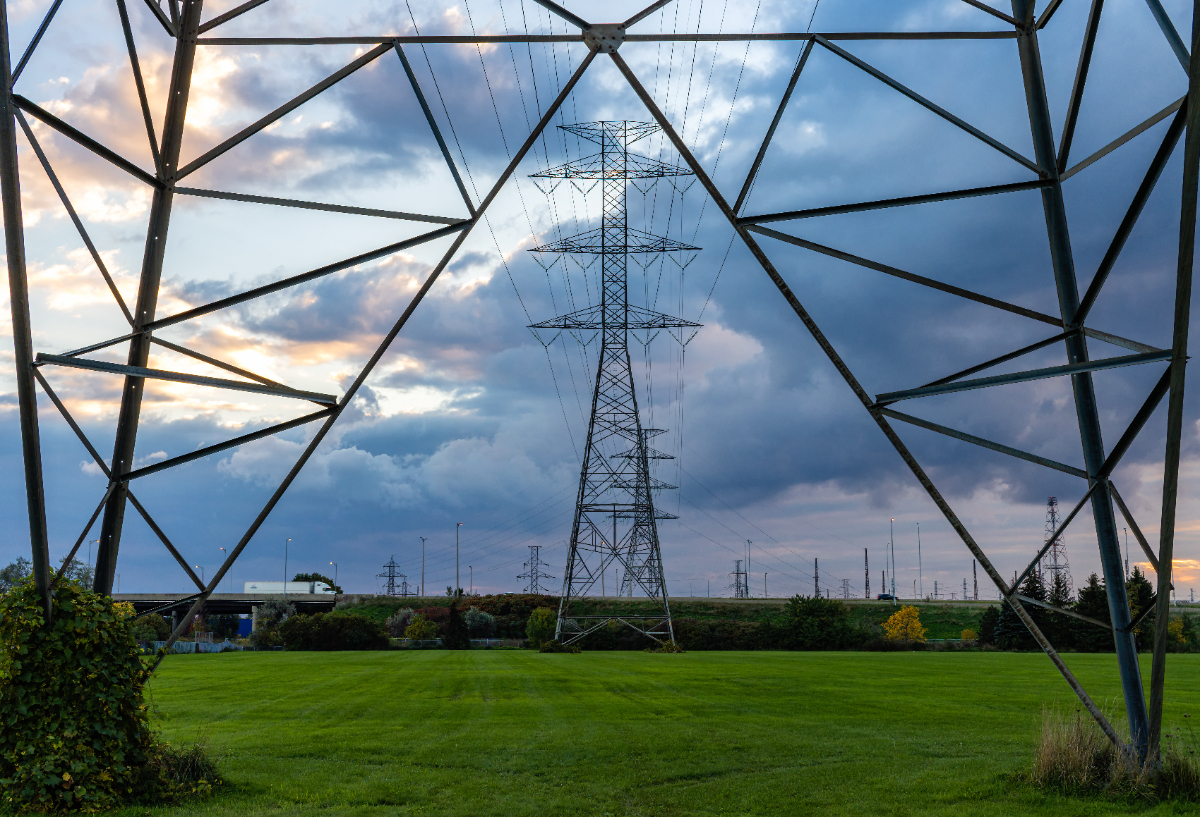 Image underneath major electrical transmission line infrastructure framing the shot, dark clouds in the sky and more transmission lines in the distance.