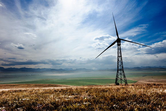 Une éolienne dans un champ sous un ciel partiellement nuageux et une chaîne de montagnes au loin
