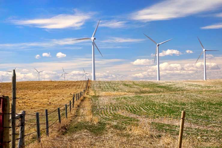 Éoliennes dans des champs cultivés séparés par une vielle clôture sous un ciel partiellement nuageux