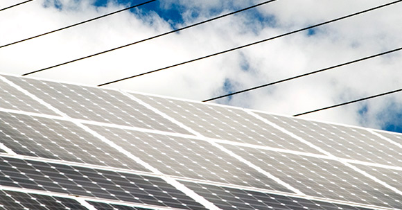 Gros plan de panneaux solaires surplombés de lignes électriques traversant un ciel nuageux.