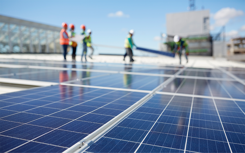 Des travailleurs portant leur EPI installent des panneaux solaires sur un toit.