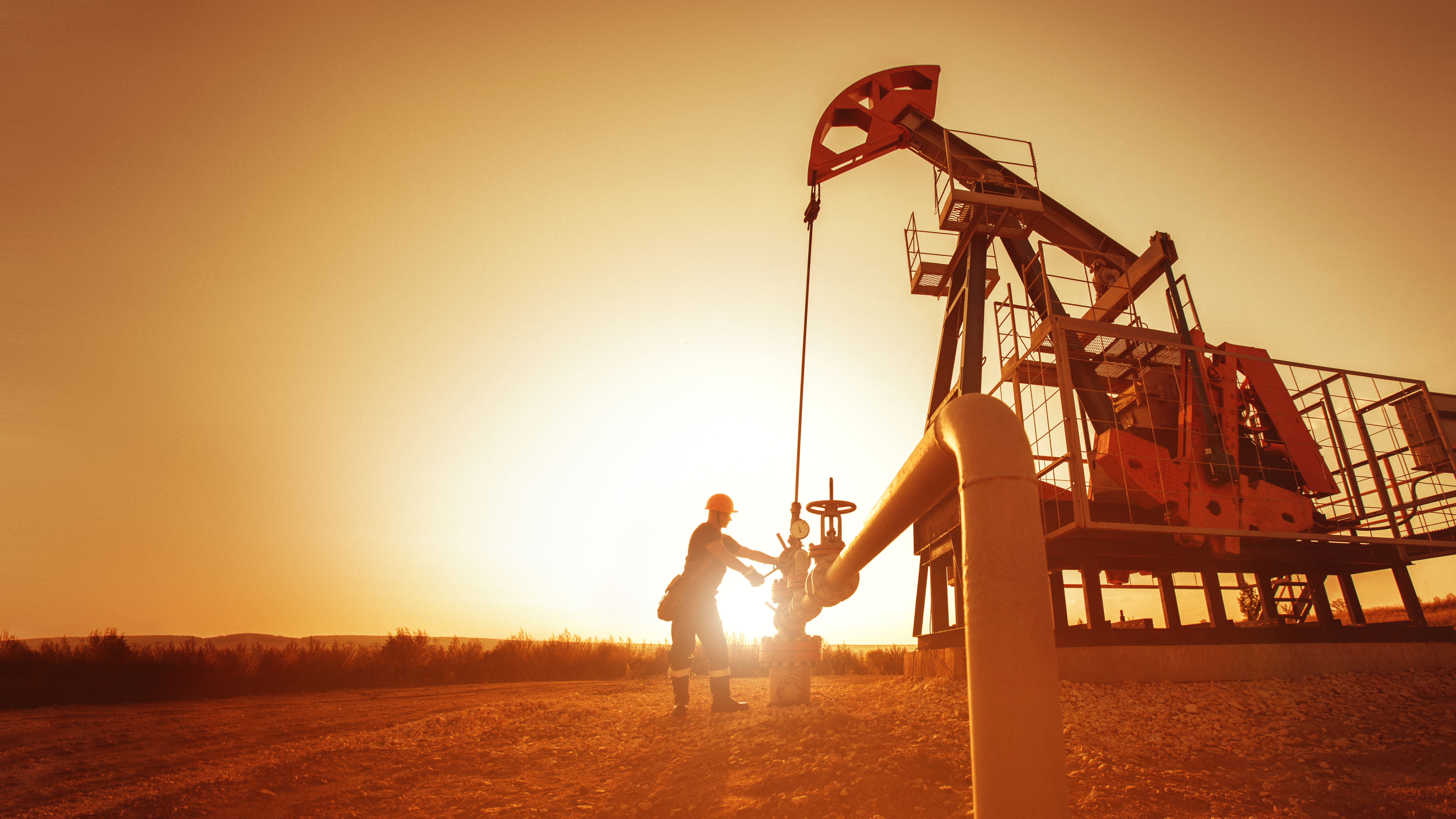 Worker maintaining oil derrick at dusk.