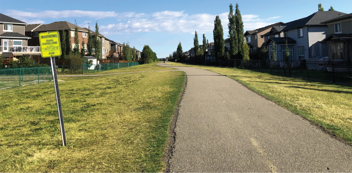 Panneau indicateur de pipeline sur une emprise près d’un sentier dans un quartier résidentiel