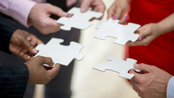 Des mains individuelles de différentes ethnies tiennent des pièces de puzzle dans le but de former un tout unifié.