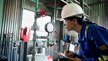 Une femme portant de l’équipement de protection individuelle est penchée vers l’avant et observe des instruments sur un chantier.