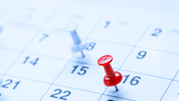 Vue latérale de dates sur un calendrier, quelques punaises, une rouge et une blanche, sont enfoncées.