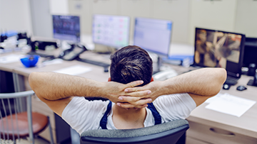 Un homme penché vers l’arrière dans un fauteuil de bureau, les mains jointes derrière la tête.